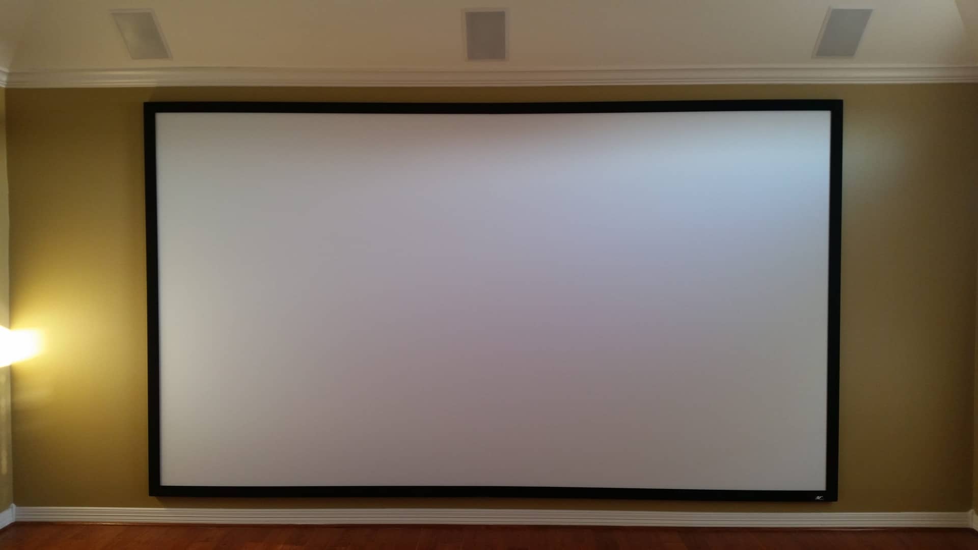 Large wall-mounted projection screen in a home theater room with warm lighting and elegant decor