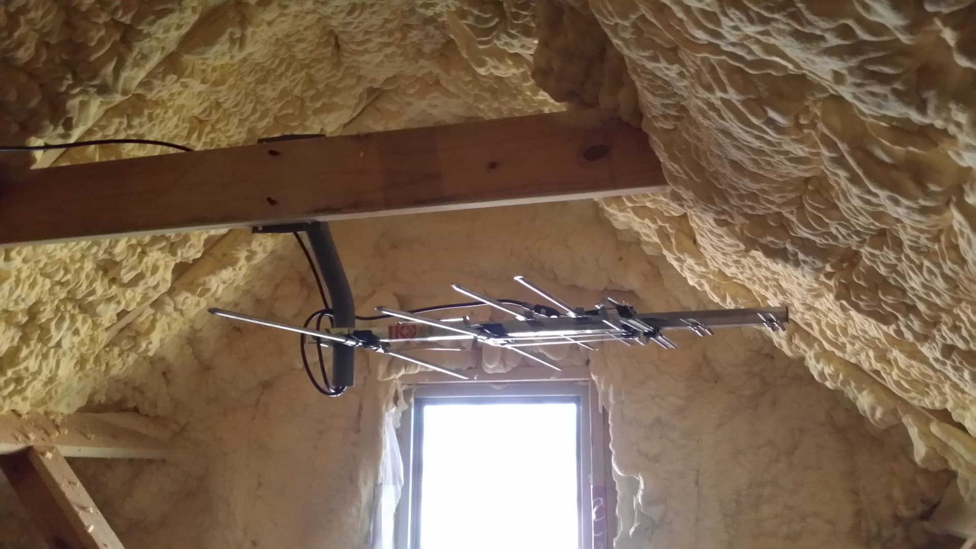 Wooden beam with cables mounted inside a rustic stone building with a visible window.