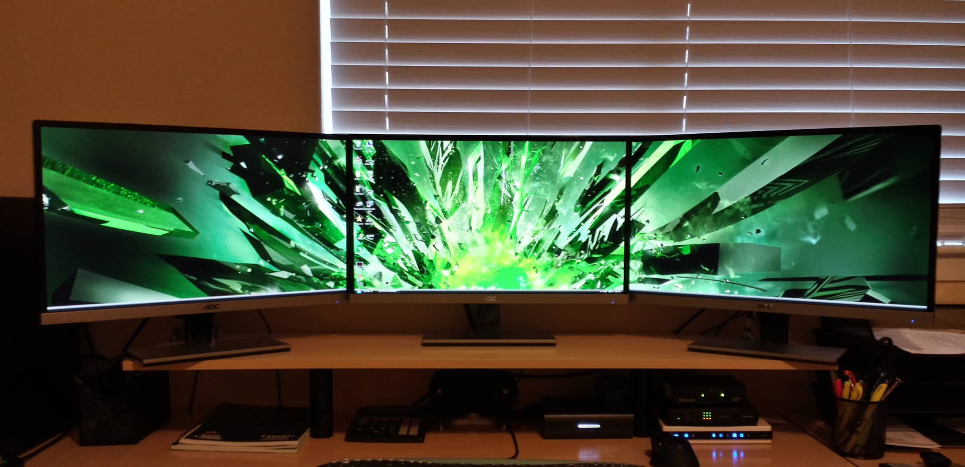A wide angle view of an ultra-wide triple monitor setup displaying a vibrant green abstract wallpaper, enhancing a modern workspace.