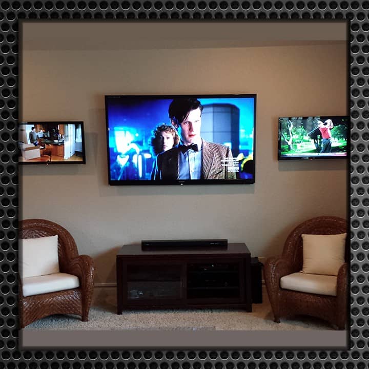 Modern living room featuring three wall-mounted TVs showing different programs, with two wicker chairs and a wooden entertainment console.