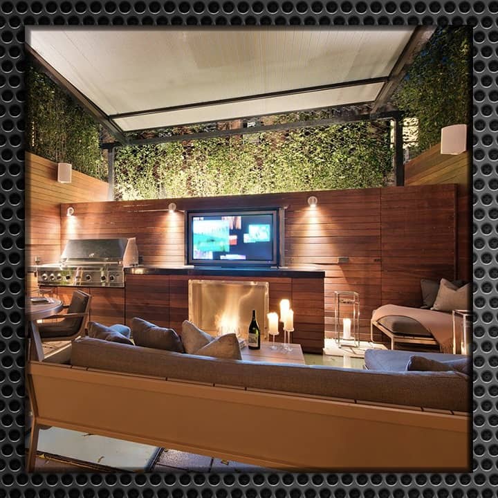 Luxurious outdoor living space with a flat-screen TV mounted on a wooden wall, surrounded by comfortable seating and atmospheric lighting