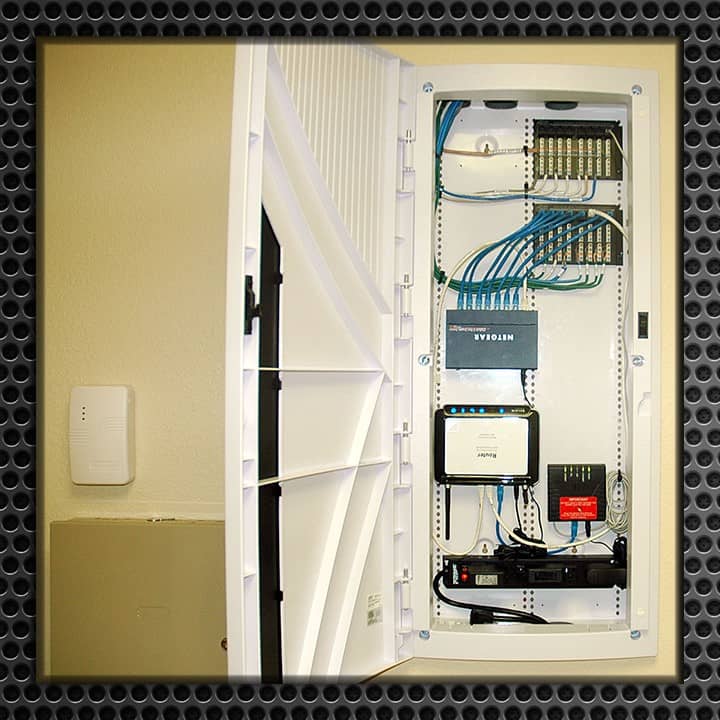 Open residential structured wiring panel displaying organized coaxial and Ethernet cables, various modules, and patch panels in a home environment.