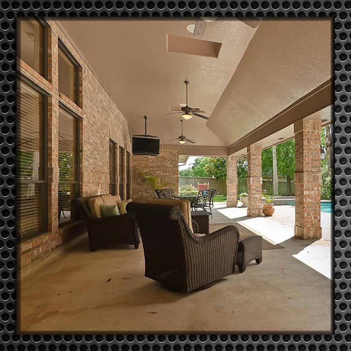 Covered outdoor patio with a ceiling-mounted TV, featuring dark wicker furniture, tiled floors, and views of the pool area