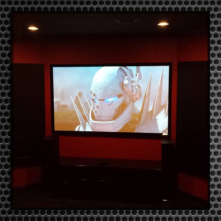 Home theater room with red backlighting featuring a large projector screen displaying a futuristic movie scene, surrounded by black walls and red LED lighting.