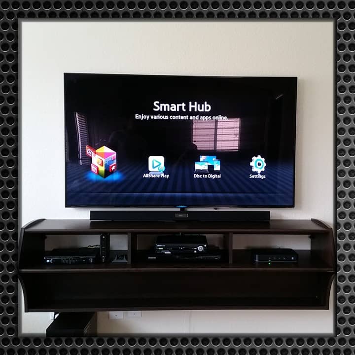 Flat-screen TV mounted on a patterned wallpaper wall in a living room, displaying a smart hub interface with app icons.
